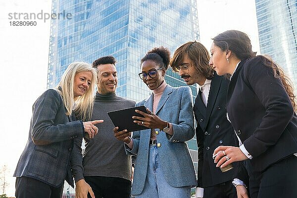 Eine Gruppe lächelnder multiethnischer Geschäftsleute schaut auf eine Tafel vor dem Glasgebäude