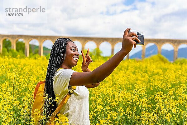 Selfie in der Natur mit einer Vintage-Kamera  ein Mädchen schwarzer Ethnie mit Zöpfen  eine Reisende  in einem Feld von gelben Blumen