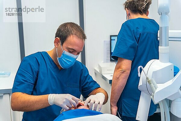 Zahnklinik  Zahnarzt und Assistentin untersuchen die Zähne einer älteren Frau  die auf dem Tisch liegt