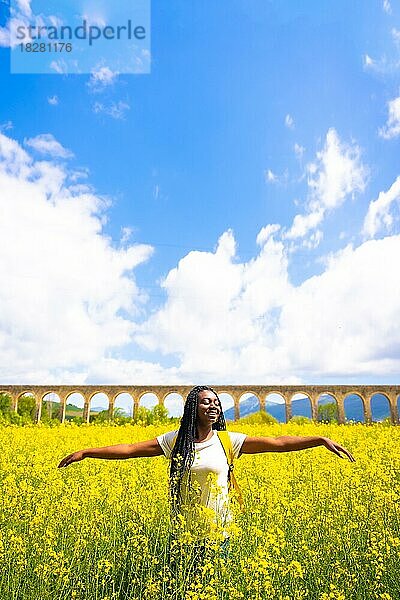 Genießen Sie den Frühling im Urlaub  schwarze ethnische Mädchen mit Zöpfen  Reisende  in einem Feld von gelben Blumen  vertikale Foto