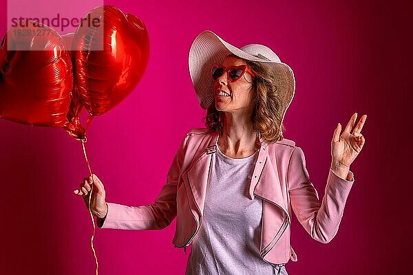 Porträt einer kaukasischen Frau  die mit einem weißen Hut in einem Nachtclub mit einigen Herzluftballons tanzt  rosa Hintergrund