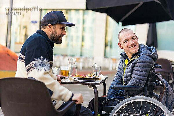 Freunde beim Essen auf der Terrasse eines Restaurants  behinderte Person  Rollstuhl