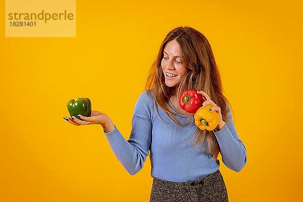 Vegane Frau lächelnd mit grünen  gelben und roten Paprika auf einem gelben Hintergrund  vegetarisches Leben