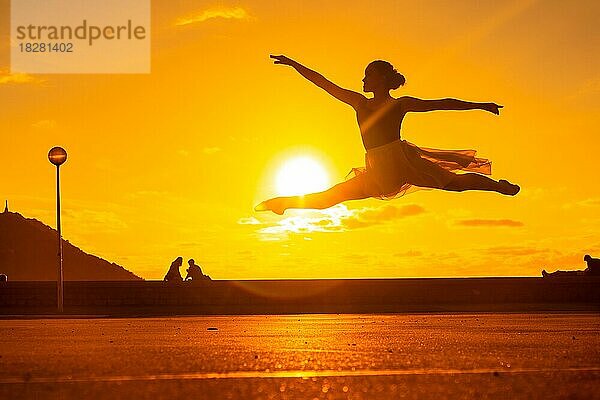 Silhouette einer jungen Tänzerin  die bei Sonnenuntergang einen Sprung am Strand vollführt und ein Tutu trägt