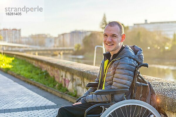 Eine behinderte Person im Rollstuhl neben einem Fluss in der untergehenden Sonne der Stadt