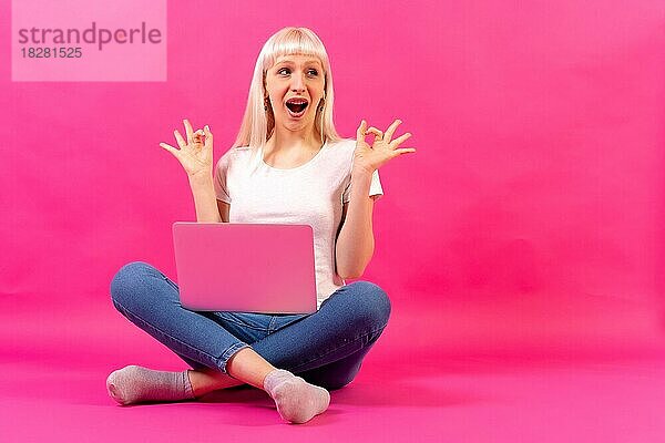 Blondes kaukasisches Mädchen mit einem Computer  Studioaufnahme auf rosa Hintergrund  Kopierraum  ok Geste