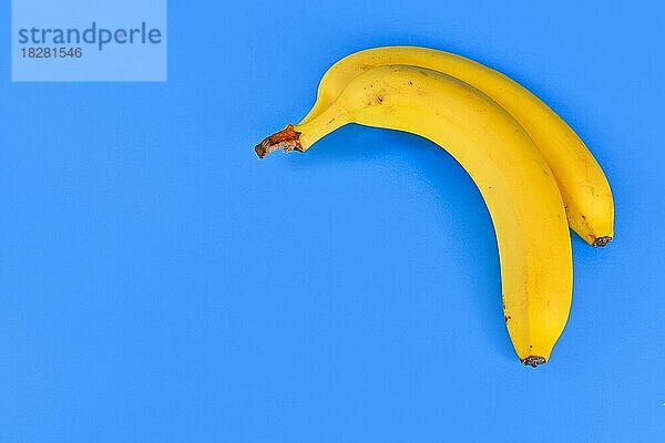 Zwei Bananenfrüchte mit Schale auf blauem Hintergrund