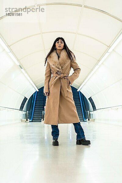 Posing eines schönen brünetten Mädchens beim Betreten der U-Bahn mit einer Jacke im Winter. Hübsche Kaukasierin geht durch den Tunnel