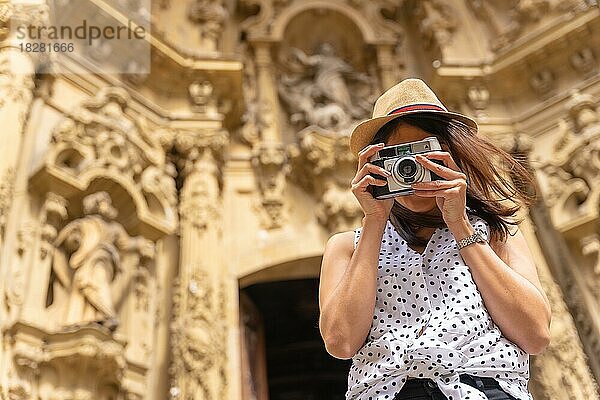 Eine Frau mit Hut  die die Stadt besichtigt und mit einer alten Kamera Fotos macht und den Sommerurlaub genießt  Konzept einer weiblichen Reisenden oder Urlauberin und Erstellerin digitaler Inhalte