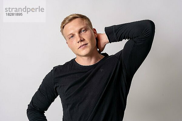Attraktives blondes deutsches Model in einem schwarzen Pullover auf weißem Hintergrund  in Mode posiert