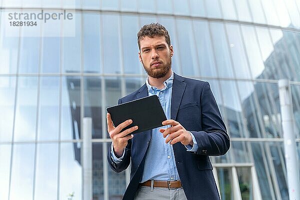 Junger männlicher Unternehmer außerhalb des Büros  der mit einem Tablet in der Hand herumläuft