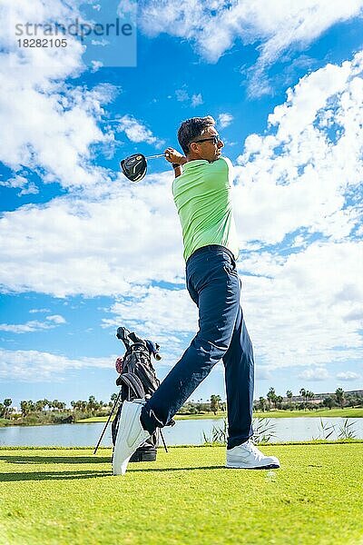 Ein Spieler spielt Golf auf dem Golfplatz und schlägt den Ball neben einem See ab  vertikales Foto