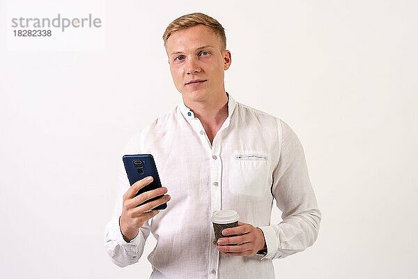 Porträt eines blonden kaukasischen männlichen Geschäftsmannes  der mit einem Telefon lächelt  auf weißem Hintergrund