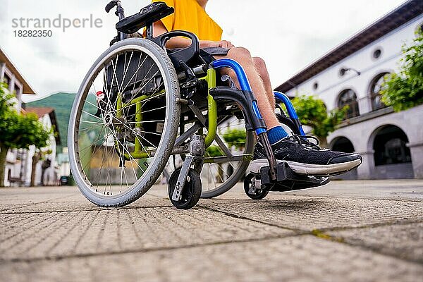 Detail einer behinderten Person in einem Rollstuhl  die über den Stadtplatz geht