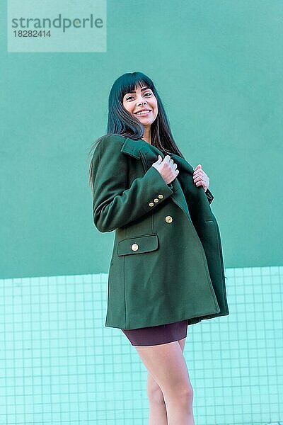Brünette Modell lächelnd in einem streetyle in einer grünen Jacke. Kaukasierin hübsch ein grüner und blauer Hintergrund