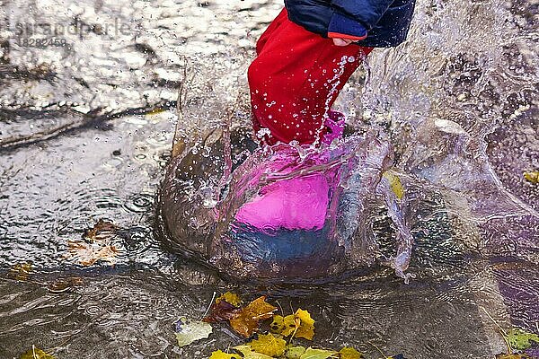 Kind spritzt mit Stiefeln und Wasserhose in einer Pfütze an einem regnerischen Tag mit Wasser