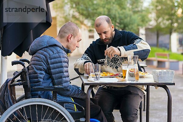 Eine behinderte Person  die mit einem Freund auf der Terrasse eines Restaurants isst und Spaß hat