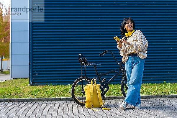 Porträt eines asiatischen Mädchens  das mit gelben Kopfhörern auf einem blauen College-Hintergrund Musik hört