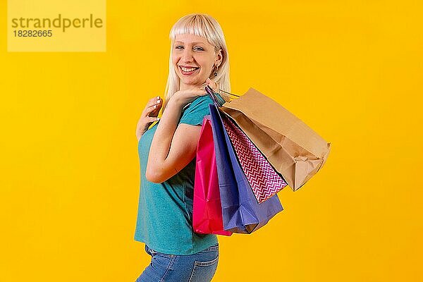 Lachende Einkaufen mit Taschen auf Verkauf  blonde kaukasische Mädchen im Studio auf gelbem Hintergrund