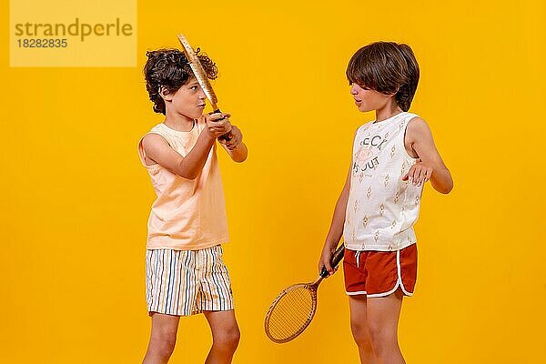 Zwei Brüder spielen Tennis und haben Spaß im Sommerurlaub  gelber Hintergrund