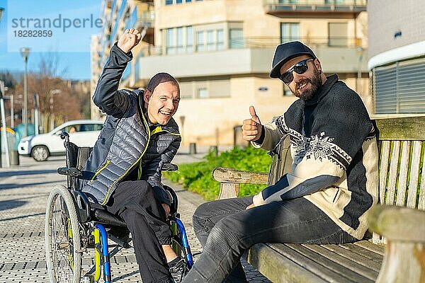 Porträt einer behinderten Person im Rollstuhl mit einem Freund  der sich auf der Straße amüsiert