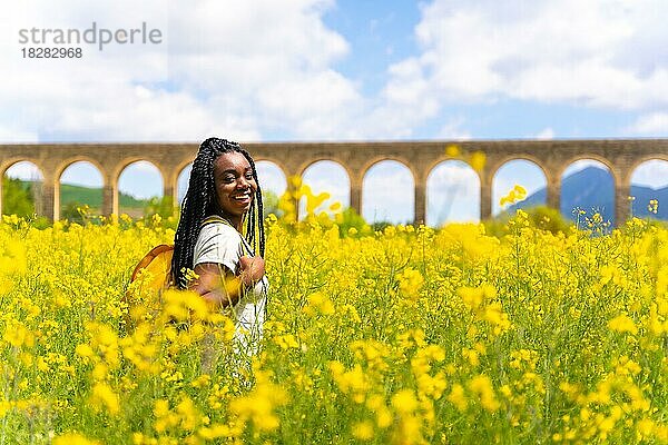 Genießen Sie den Frühling im Urlaub  schwarze ethnische Mädchen mit Zöpfen  Reisende  in einem Feld von gelben Blumen