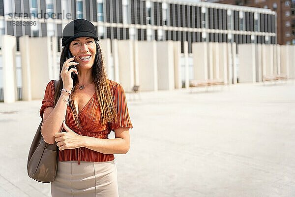 Eine Geschäftsfrau vor dem Büro  die einen Anruf tätigt  mit braunem Hemd und schwarzem Hut