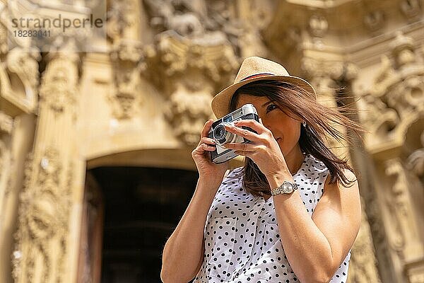 Eine Frau mit Hut  die die Stadt besichtigt und Fotos mit einer alten Kamera macht  die Sommerferien genießend  Konzept einer weiblichen Reisenden und Schöpferin digitaler Inhalte