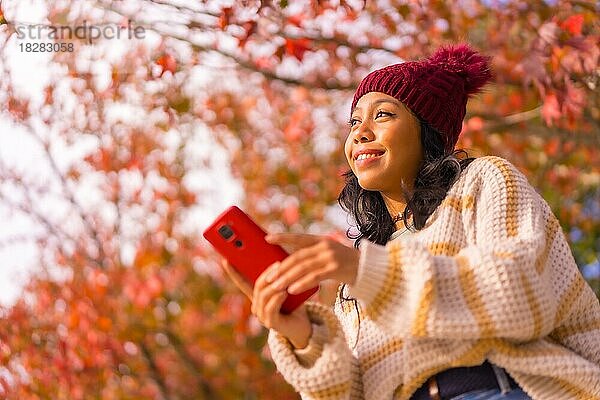Porträt einer asiatischen Frau im Herbst mit einem Handy in einem Wald aus roten Blättern  Technik