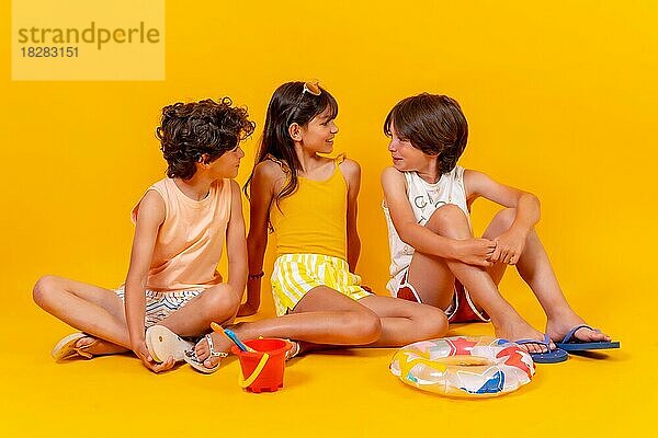 Porträts von Kindern  die auf dem Boden sitzen und die Ferien mit Spielzeug genießen  gelber Hintergrund