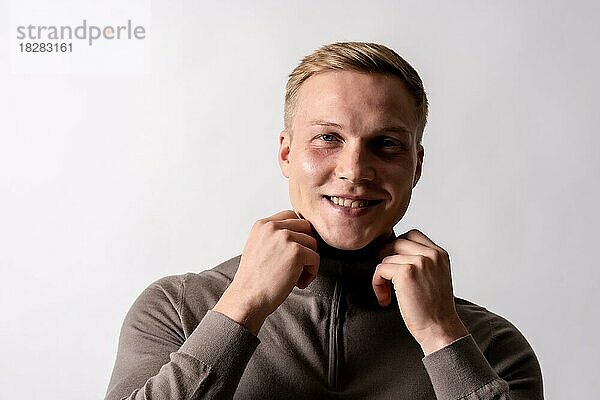 Portrait eines attraktiven blonden deutschen Models mit braunem Pullover auf weißem Hintergrund  lächelnd