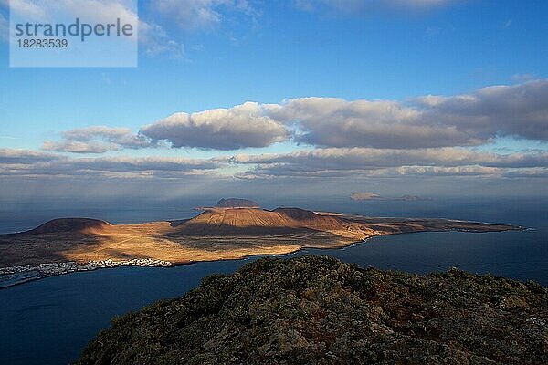 Wunderschönes weiches  winterliches Morgenlicht  Licht- und Schattenspiel  blauer Himmel  grauweiße Wolken  Mirador del Rio  La Graciosa  Siedlung und Hafen  Felskante im Vordergrund  Nordküste  Lanzarote  Kanarische Inseln  Spanien  Europa