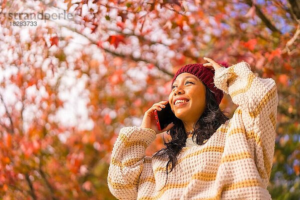 Porträt einer asiatischen Frau im Herbst mit einem Mobiltelefon  das in einem Wald aus roten Blättern telefoniert  Technik