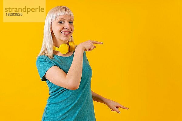 Zeigen Anzeigen nach rechts mit Kopfhörer  blonde kaukasische Mädchen auf gelbem Hintergrund Studio