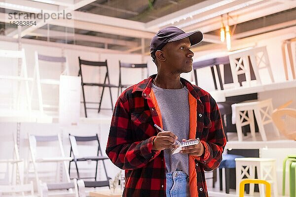 Schwarzer ethnischer Mann beim Einkaufen in einem Möbelhaus  der sich Stühle ansieht und auf die Preise achtet