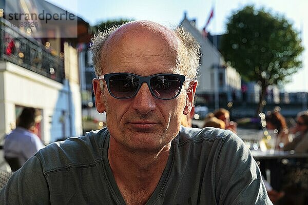 Best Ager  Portrait mit Sonnenbrille  leger  unrasiert  sitzt im Biergarten  Norwegen  Europa