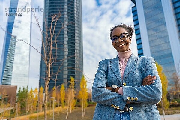 Schwarze ethnische Geschäftsfrau oder Führungskraft mit Brille  die mit verschränkten Armen in einem Gewerbegebiet steht