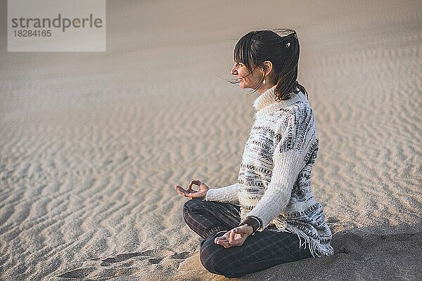 Seitenansicht einer Frau  die sich am Strand an den Händen fasst. Namaste-Pose