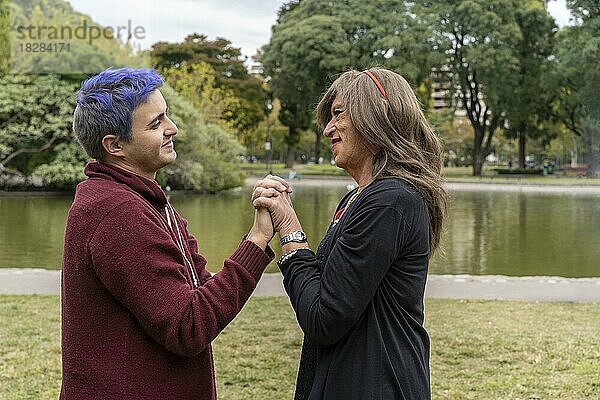 Transgender-Frau und ihr schwuler Sohn halten sich an den Händen und schauen sich liebevoll in einem Park an