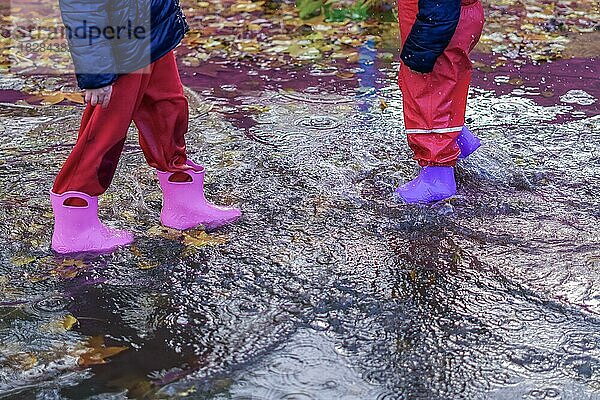 Zwei Kinder  die an einem regnerischen Tag mit ihren Stiefeln durch eine Wasserpfütze laufen