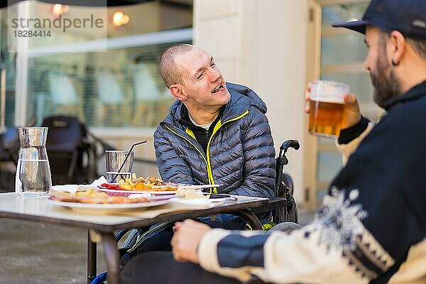Eine behinderte Person isst und lächelt mit einem Freund  der Spaß hat  Terrasse eines Restaurants