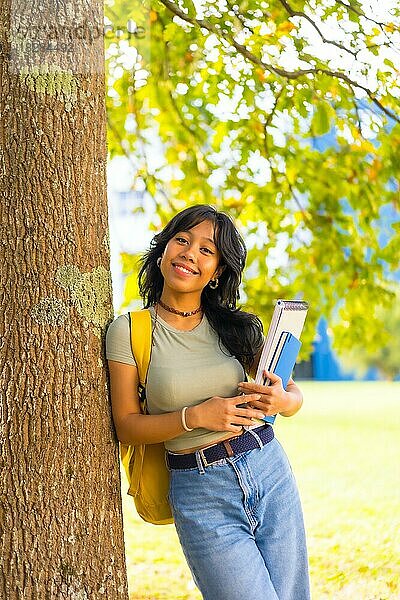 Asiatisches Mädchen auf dem Campus  lächelnd an der Universität unter einem Baum mit einem Block in der Hand