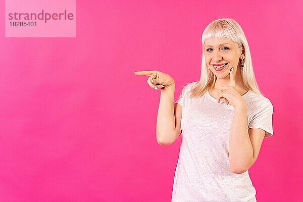 Blondes kaukasisches Mädchen Studioaufnahme auf rosa Hintergrund  Kopierraum  lächelnd nach links zeigend