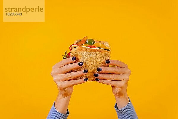 Hände einer Frau mit einem Sandwich auf einem gelben Hintergrund  gesundes und vegetarisches Essen