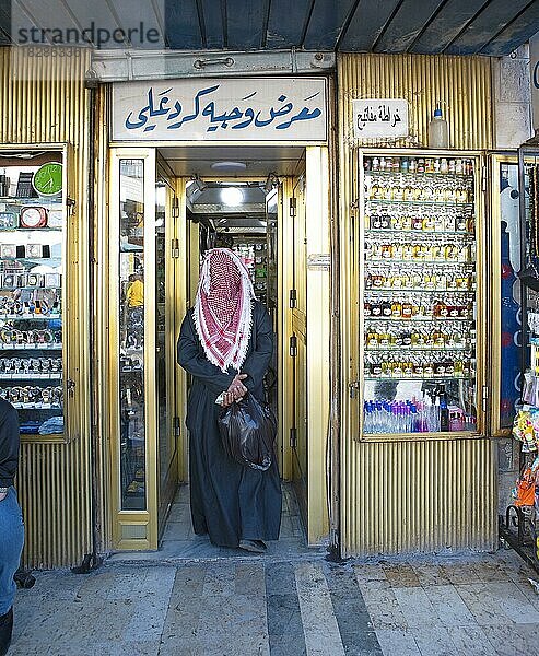 Mann mit dem traditionellen Thobe auf dem Kopf und Geld in der Hand betritt ein Geschäft  Amman  Jordanien  Asien