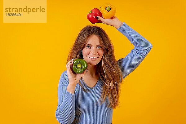 Vegetarische Frau mit grünen  gelben und roten Paprikaschoten auf gelbem Hintergrund  gesunde Ernährung