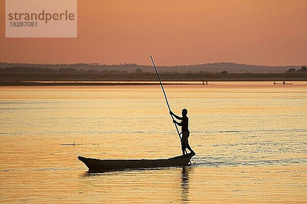 Silhouette eines madagassischen Fischers  der auf dem Tsiribihina  Tsiribinha-Fluss bei Sonnenuntergang in Menabe  Madagaskar  Südostafrika  eine Piroge  Piragua  Piraga  mit einer Stange stößt  Afrika