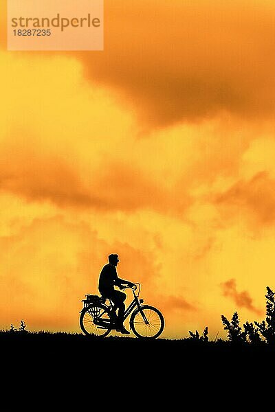 Männlicher Radfahrer fährt sein Fahrrad gegen orange Sonnenuntergang Himmel im Sommer silhouettiert