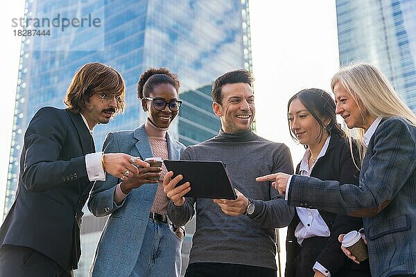 Eine Gruppe multiethnischer Geschäftsleute in einem Gewerbegebiet schaut lächelnd auf ein Tablet