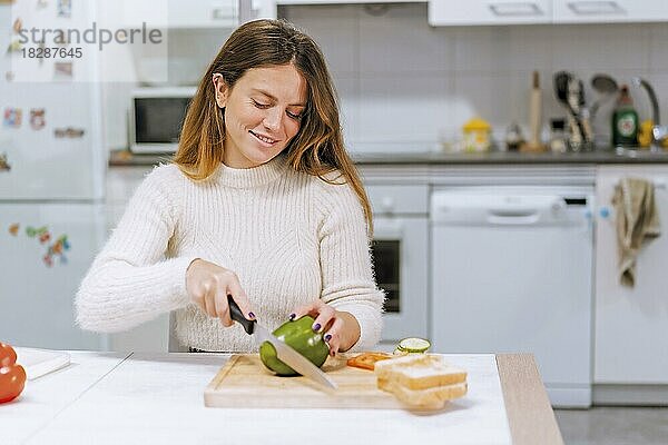 Vegetarische Frau  die zu Hause in der Küche ein Gemüsesandwich zubereitet und grüne Paprika schneidet
